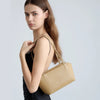 A model holds a gold leather mini shoulder bag with adjustable straps against a light gray background.