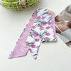 Un foulard pour cheveux en soie floral rose et blanc est exposé à côté d'un bol de pommes vertes.