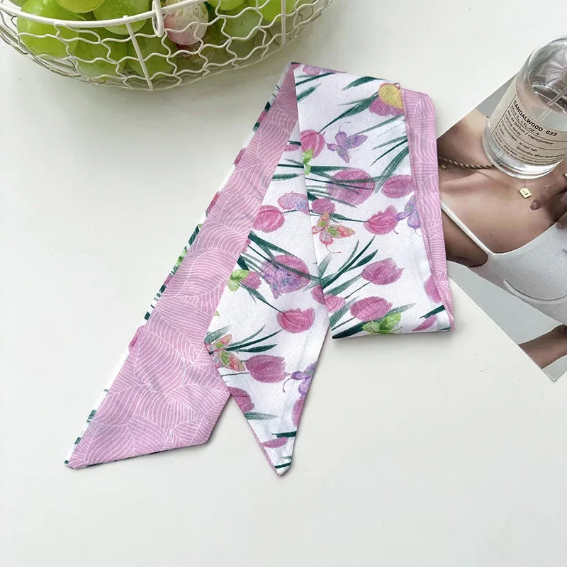 Un foulard pour cheveux en soie floral rose et blanc est exposé à côté d'un bol de pommes vertes.