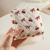 A hand holds a quilted storage pouch with a red cherry and bow print on a white background.