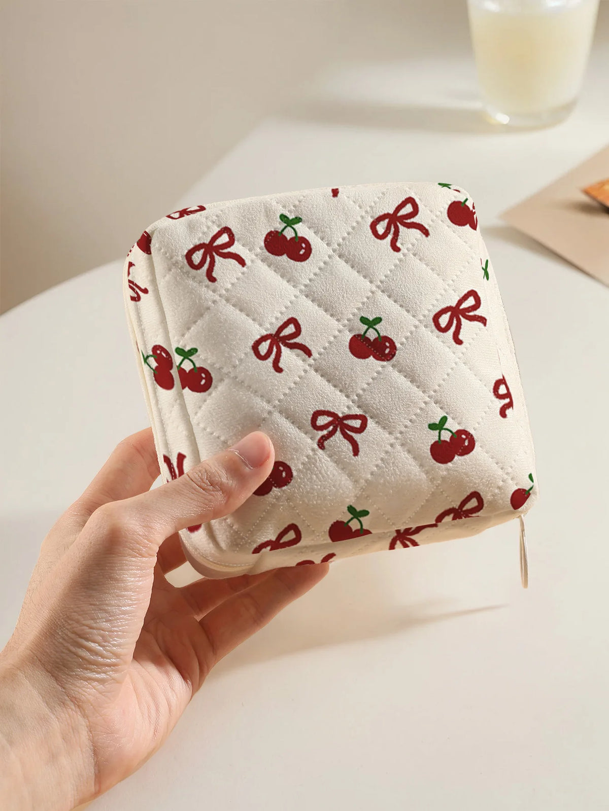 A hand holds a quilted storage pouch with a red cherry and bow print on a white background.