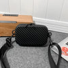 A black quilted shoulder bag with a black strap resting on a gray carpet next to a wooden surface.