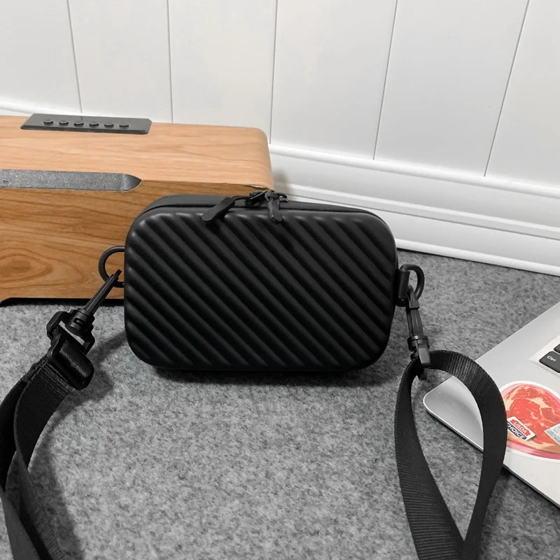 A black quilted shoulder bag with a black strap resting on a gray carpet next to a wooden surface.