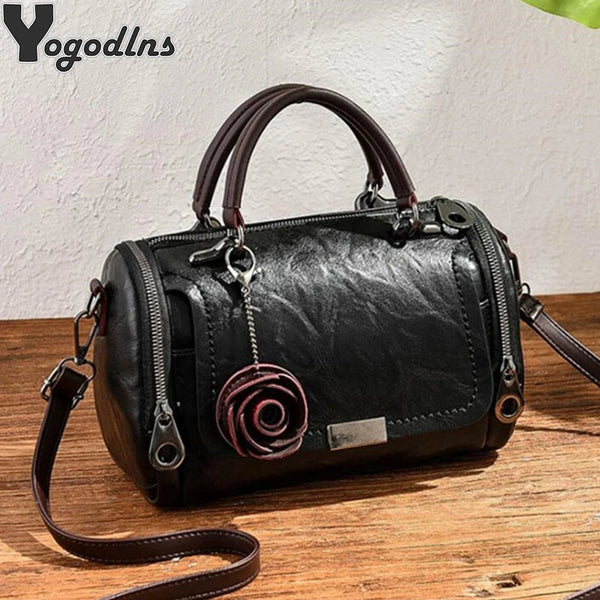Schwarze Kunstleder-Schultertasche mit rosa Anhänger und braunem Lederriemen.