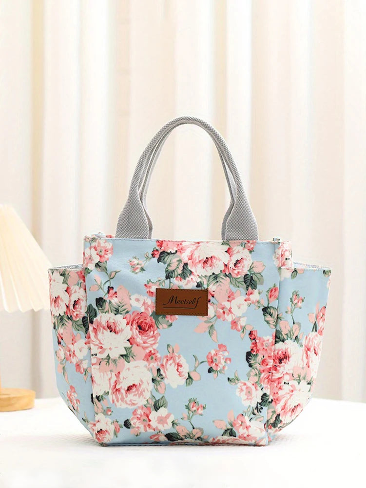 Bolsa térmica estampada floral azul claro con asas grises sobre una superficie blanca.