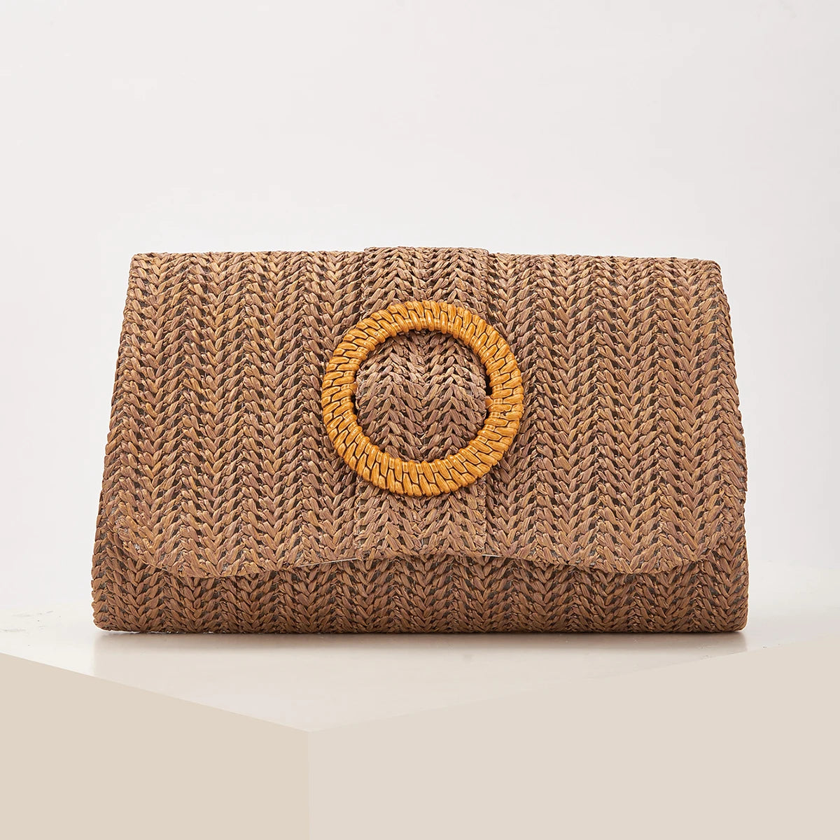 A woven straw envelope clutch in a natural brown color with a circular detail.