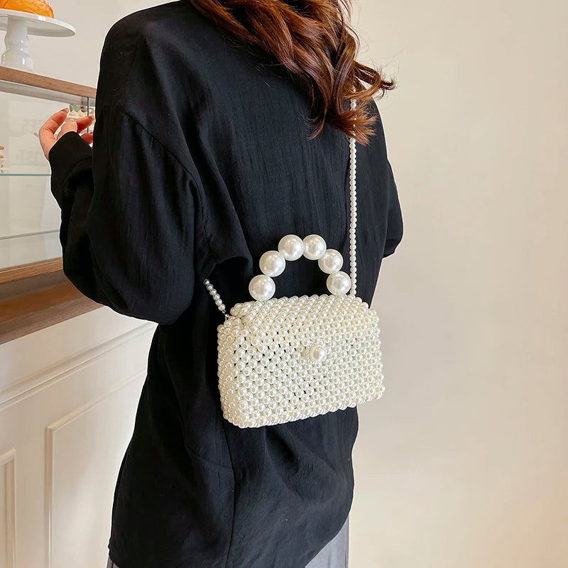 A person wearing a black oversized shirt holds a white pearl beaded clutch bag with a long strap.