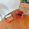 A red luminous sand effect earphone case for AirPods resting on a wooden surface next to a woven basket.