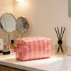 Sac de rangement cosmétique rayé rose et orange sur un comptoir blanc dans une salle de bain bien éclairée.