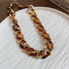 A gold-toned interlocking chain necklace featuring a leopard print design displayed on a white plate.