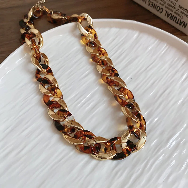 A gold-toned interlocking chain necklace featuring a leopard print design displayed on a white plate.