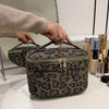 A dark brown leopard print faux suede cosmetic bag is being held by a hand on a white surface.