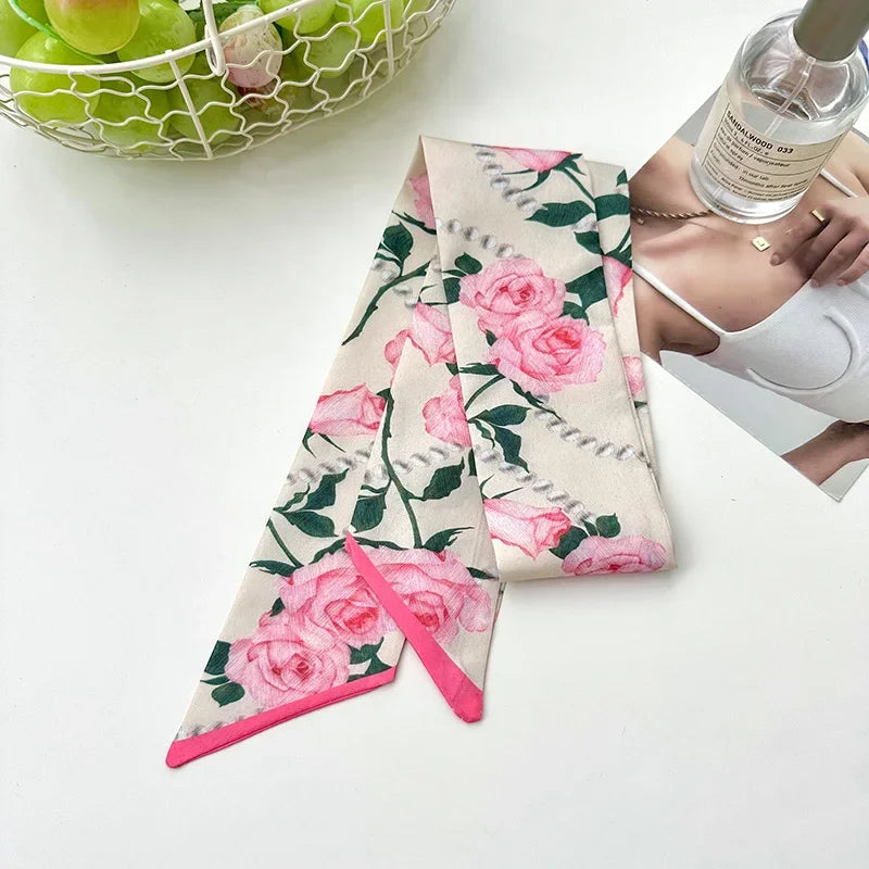 Écharpe de soie florale rose et verte pliée sur une surface blanche à côté d'une bouteille en verre.