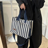 Une personne tient un sac bandoulière en toile rayée bleu marine et blanc sur un fond clair.