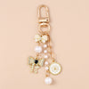 Gold-toned pearl bow heart keychain with a circular charm