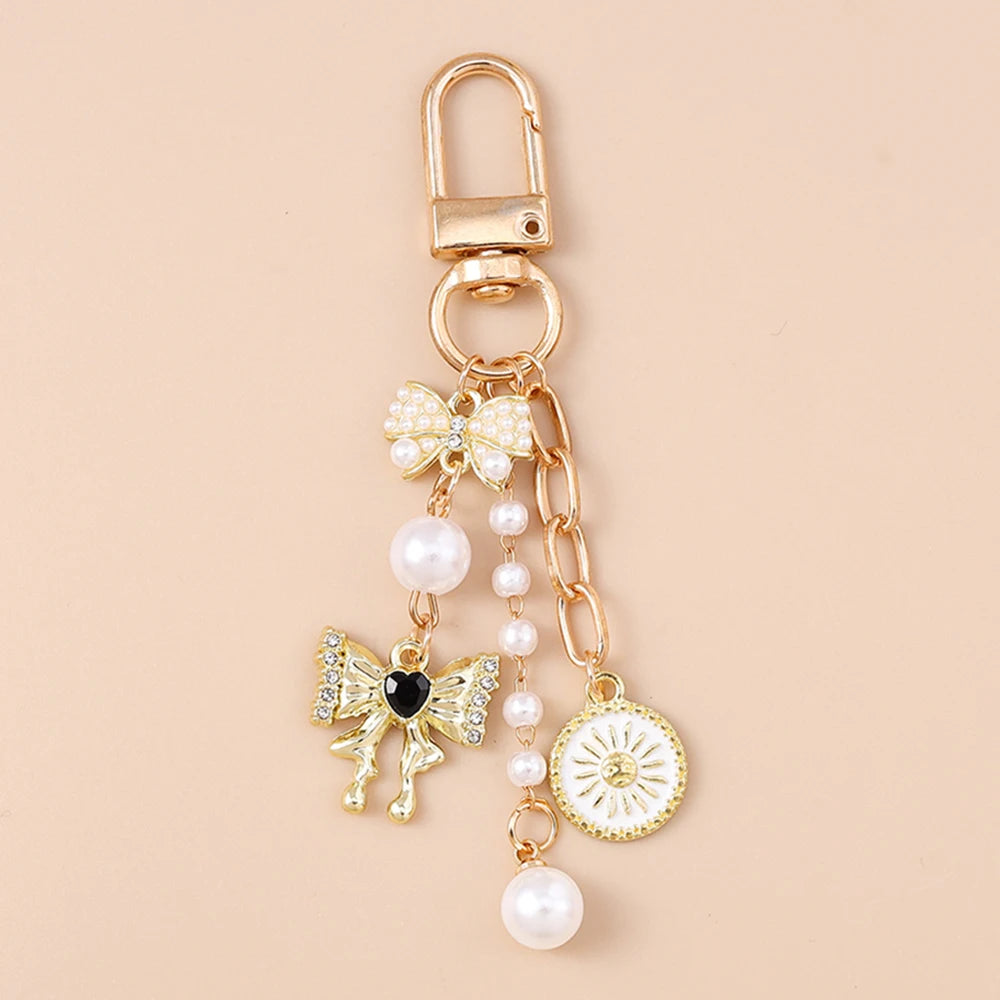 Gold-toned pearl bow heart keychain with a circular charm