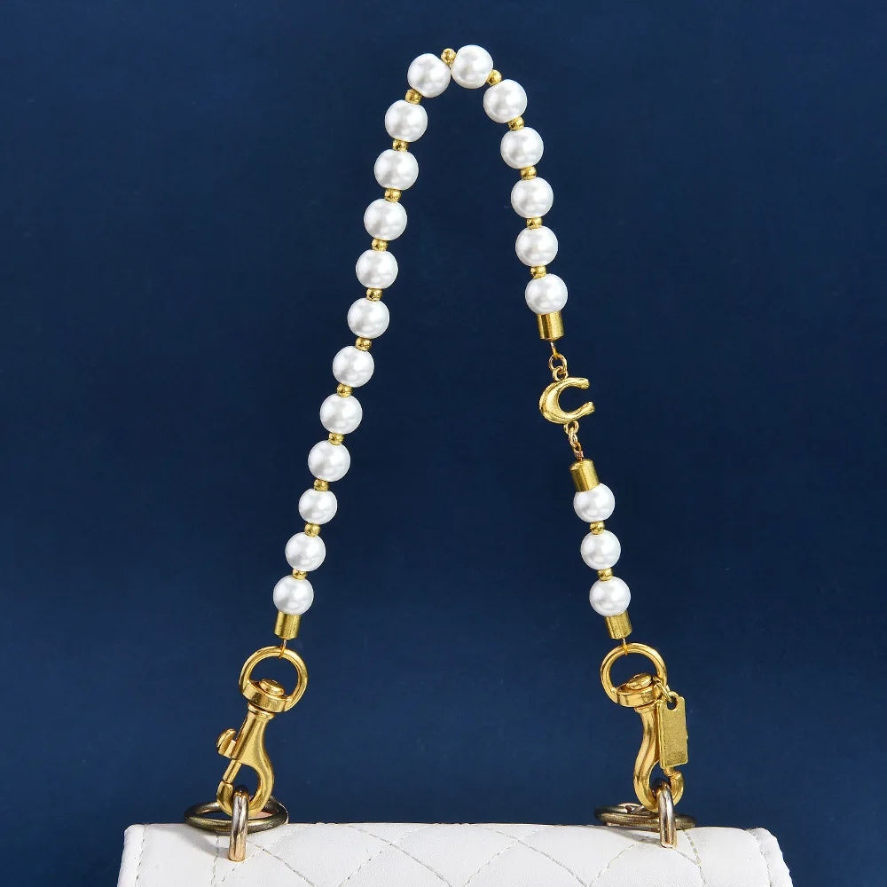 A pearl and gold letter charm necklace displayed on a white quilted bag.