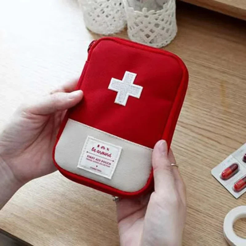 A hand holds a red portable first aid kit storage bag with a white cross emblem on a light background.