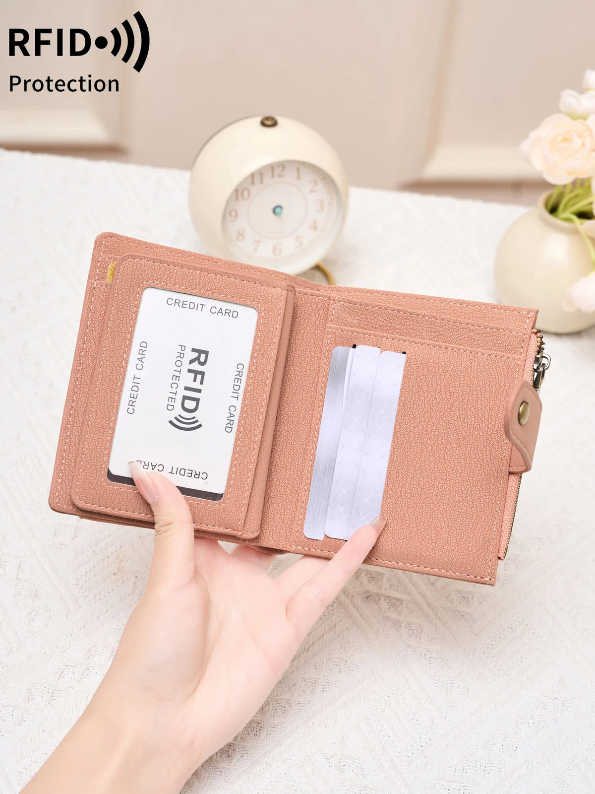 A hand holds a pink RFID-blocking compact bifold zipper wallet next to a white clock.