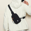 A white jacket features a black nylon sling crossbody bag with an orange detail on the front.