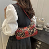 Une femme tient un sac à main en similicuir léopard rouge contre une robe gris foncé.
