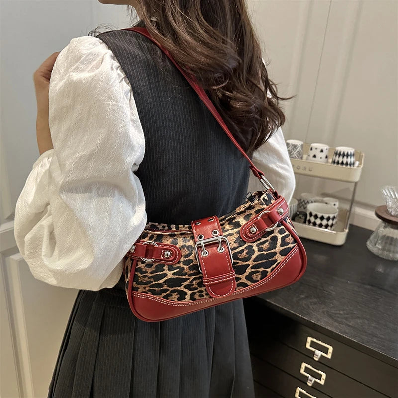 Une femme tient un sac à main en similicuir léopard rouge contre une robe gris foncé.