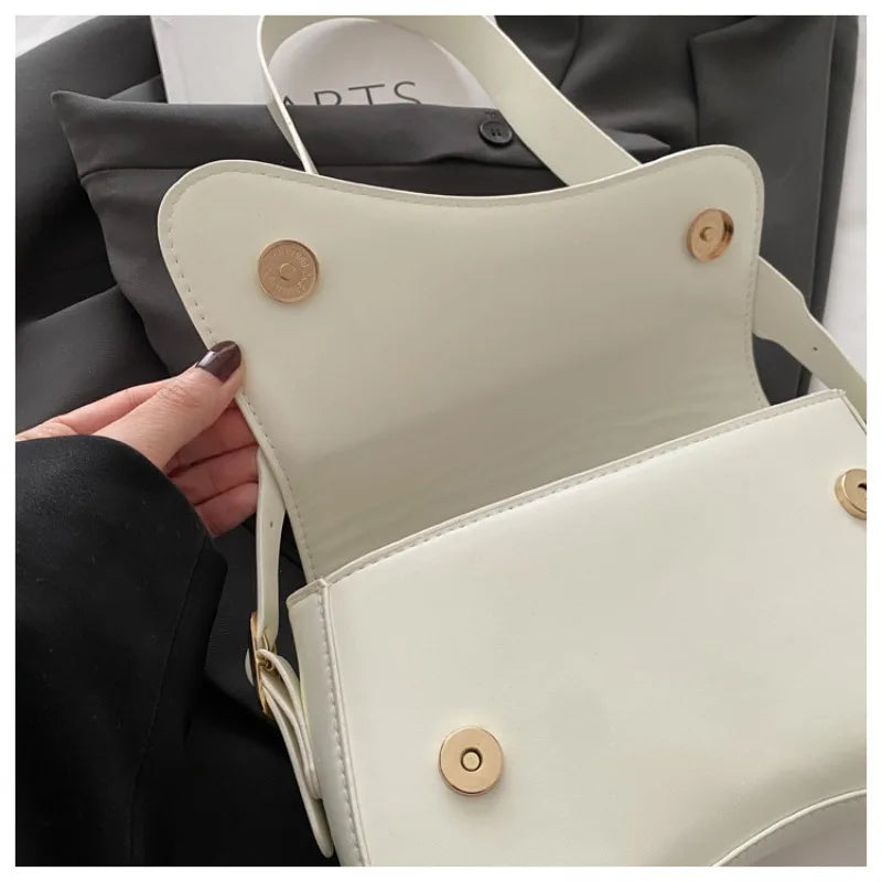 A close-up of a cream vintage curved flap shoulder bag with light leather straps and gold-toned hardware.