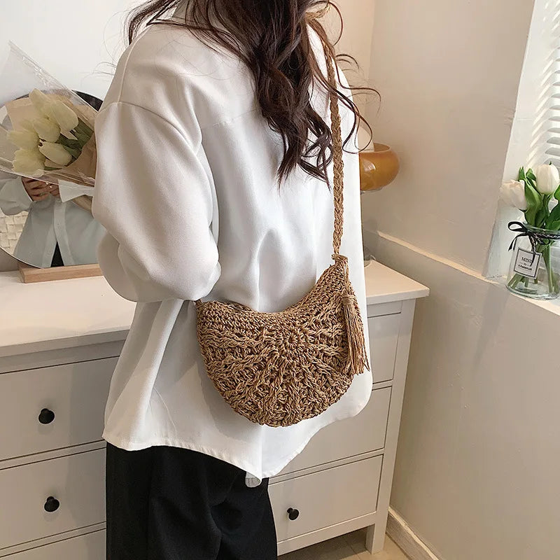 A woman wearing a white oversized shirt and black pants holds a handmade rattan straw crossbody bag.