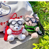 A white fluffy bear plush toy wearing a red sweater and black camera and glasses, resting on a light-colored surface.