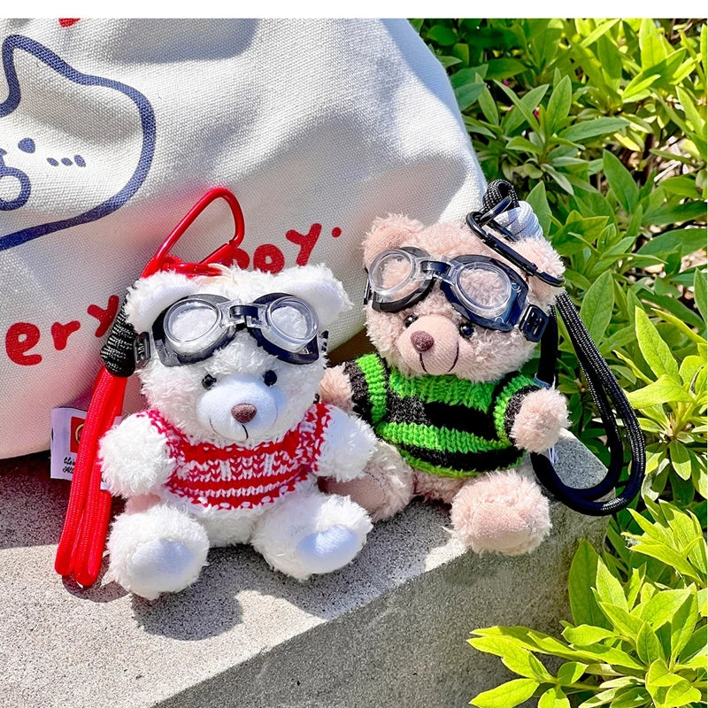 A white fluffy bear plush toy wearing a red sweater and black camera and glasses, resting on a light-colored surface.