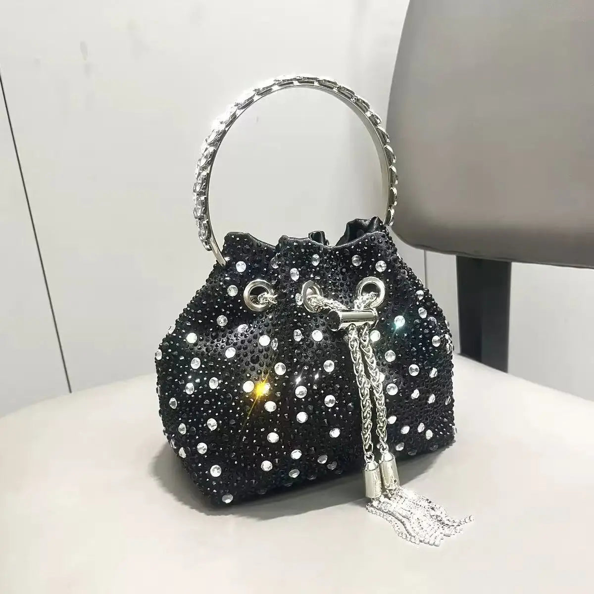 A black crystal-embellished evening clutch with a silver chain handle resting on a white surface.