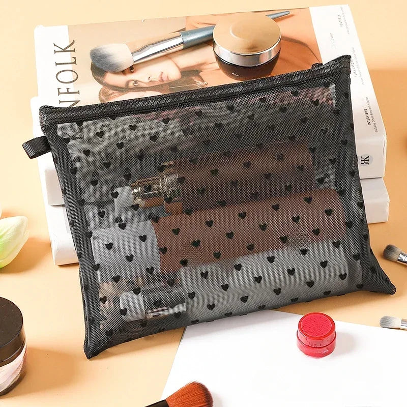 A black mesh cosmetic storage pouch is shown open, containing makeup brushes and other beauty tools on a light brown surface.