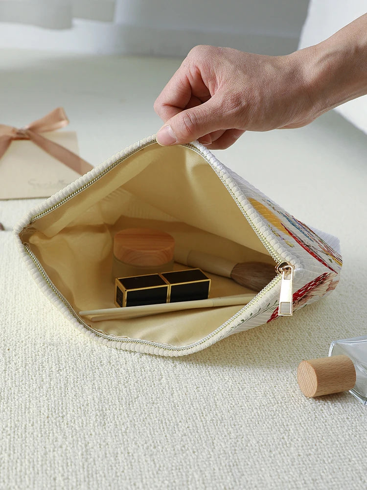 A hand is opening a beige makeup bag with a floral print to reveal wooden makeup brushes inside.