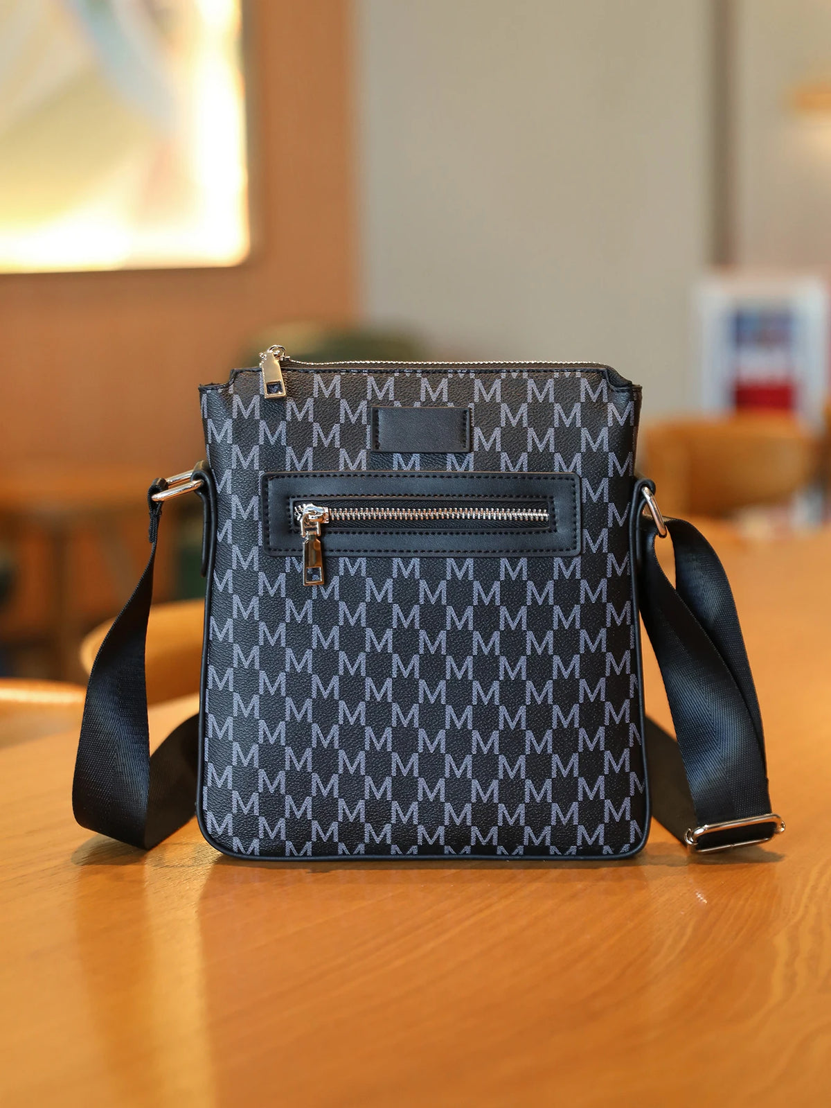 A dark gray men's lightweight crossbody sling bag with a zippered front pocket resting on a wooden surface.