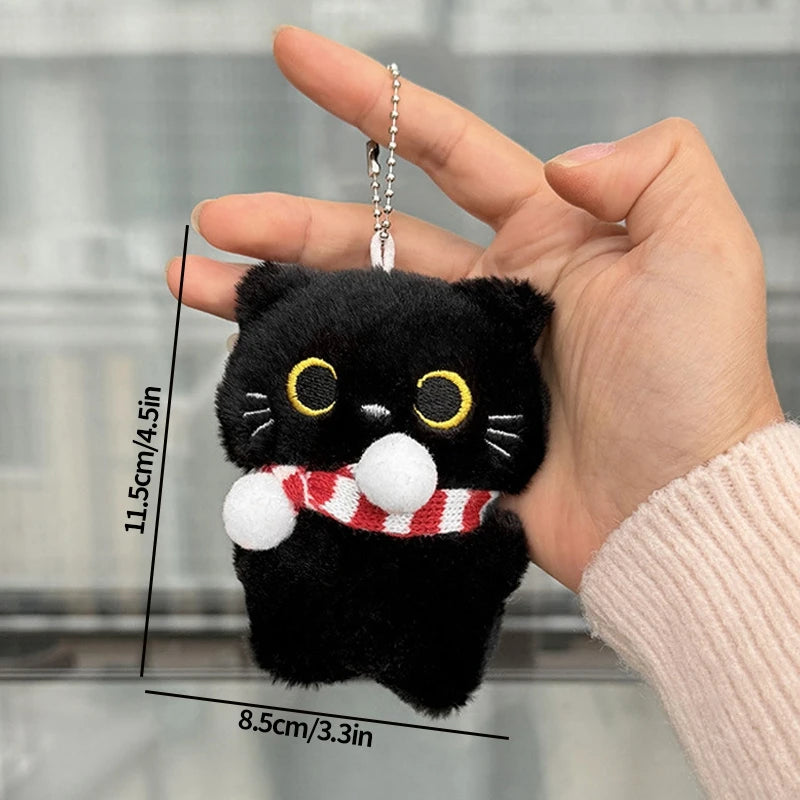 Una mano sostiene un dije/llavero de gato de peluche negro contra un fondo desenfocado.