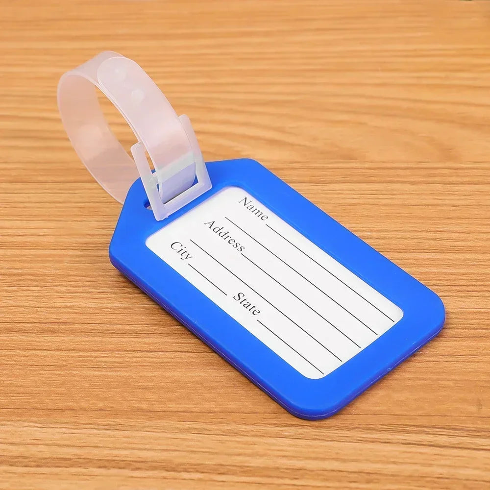 A blue luggage tag with a clear plastic holder and a strap, lying on a wooden surface.