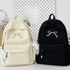 A cream-colored backpack with a bow detail next to a black backpack.