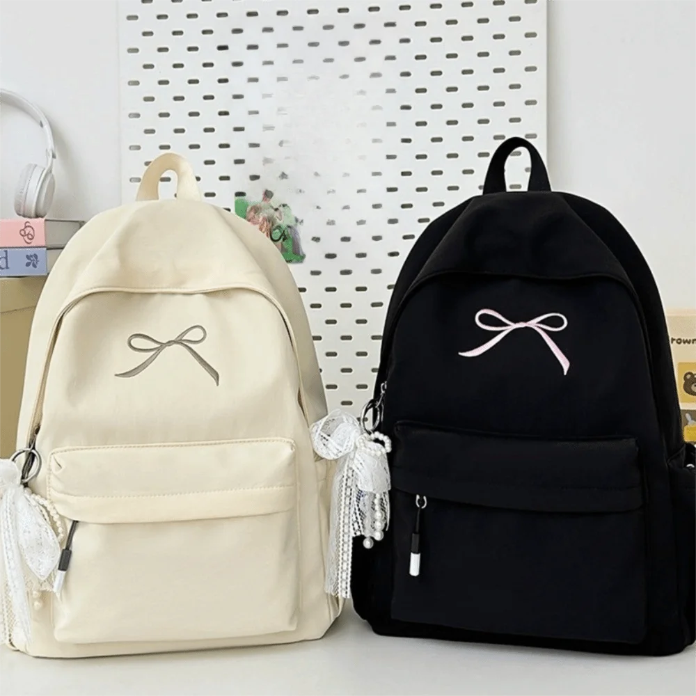 A cream-colored backpack with a bow detail next to a black backpack.