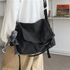 Bolso cruz de lona negra colgando de una camisa blanca, con un dije gris adjunto.