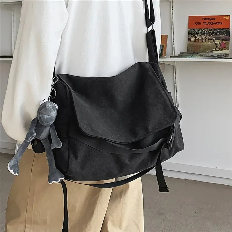 Un bolso cruz de lona negra colgado de una camisa blanca, con un peluche gris unido.