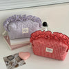 A red and white checkered makeup pouch with a ruffled lace trim is displayed next to a lavender patterned pouch.