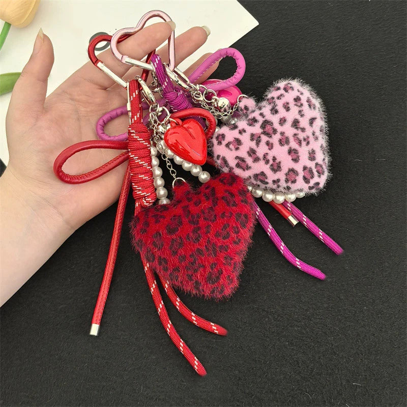 A hand holds a collection of heart-shaped charm keychains featuring various colors and leopard print faux fur.