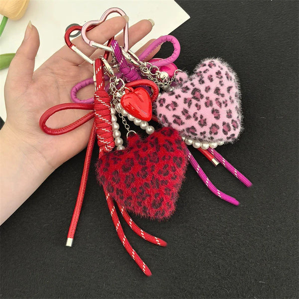 A hand holds a collection of heart-shaped charm keychains featuring various colors and leopard print faux fur.