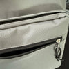 A close-up of a light gray canvas backpack showing a zippered pocket detail.