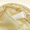 A white tube of product is placed inside a light yellow quilted puffer makeup bag.