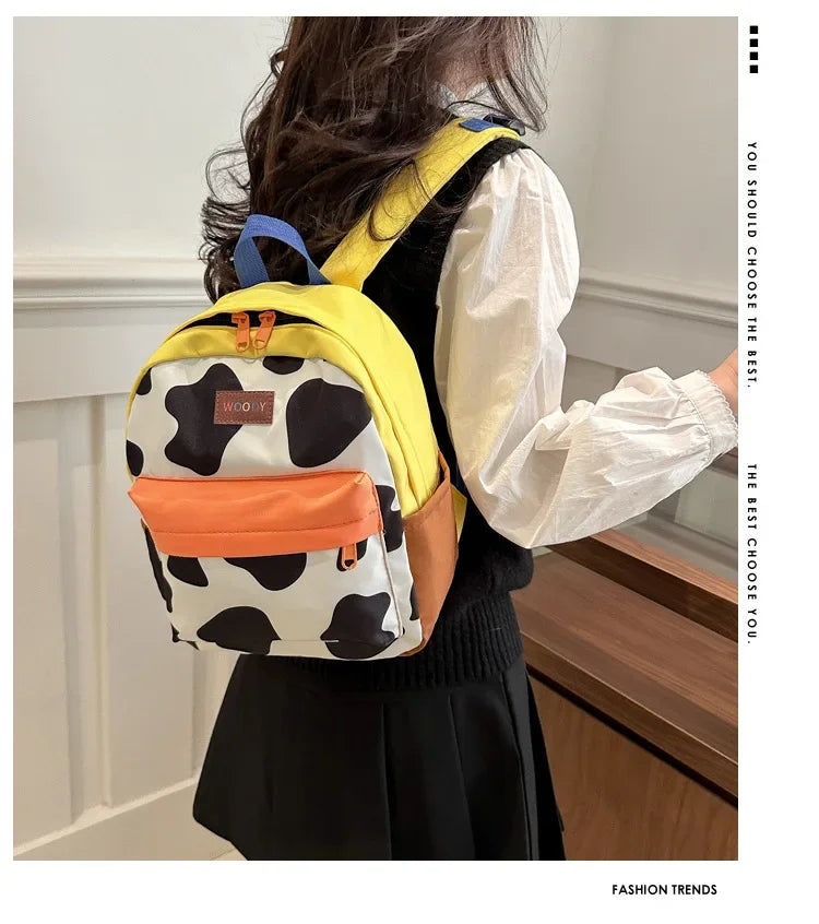 A woman is shown from the back wearing a yellow and white cow print fashion backpack.