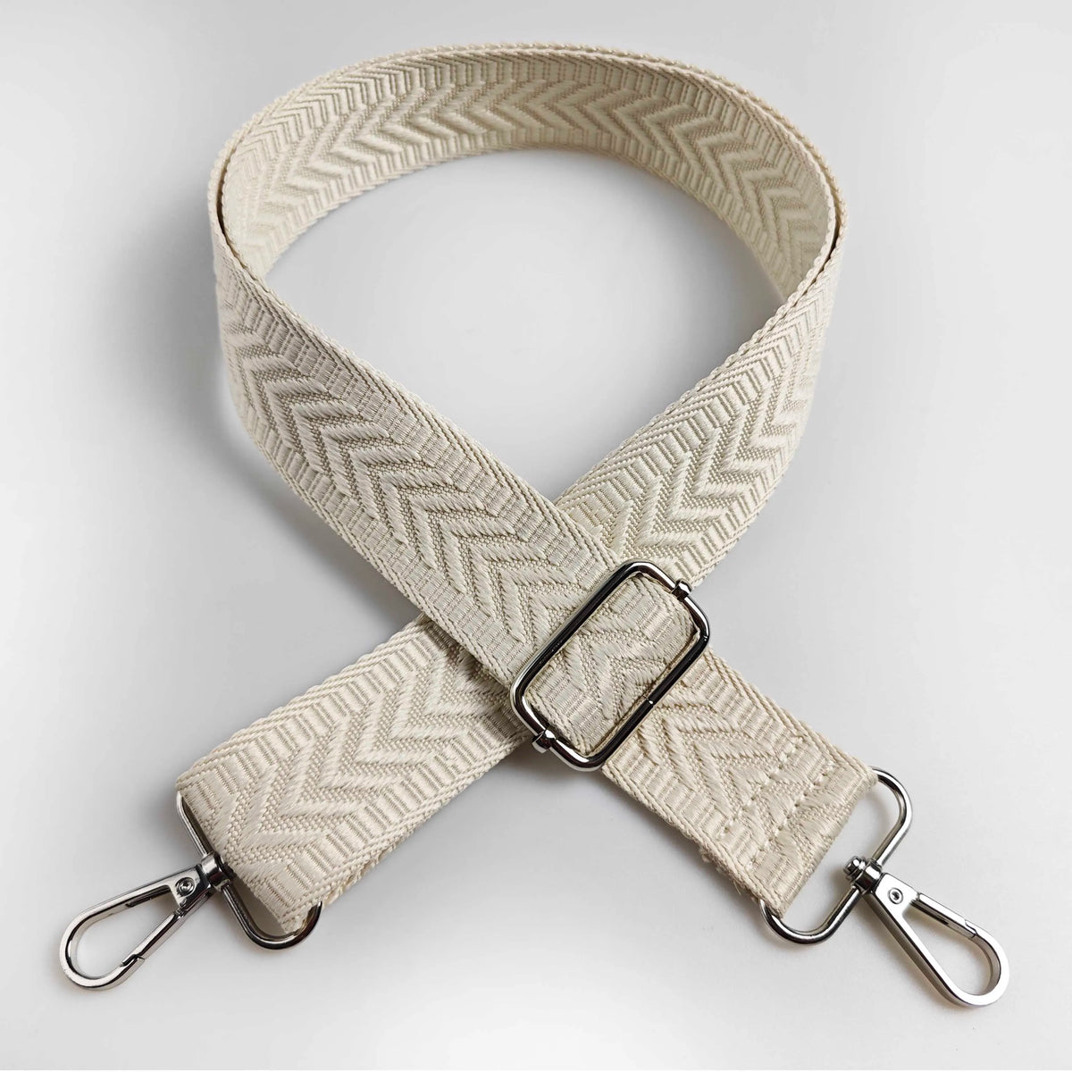 A beige woven strap with an arrow jacquard pattern, folded and displayed against a light gray background.
