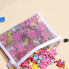A clear mesh zipper pouch filled with colorful puzzle pieces on a light beige background.