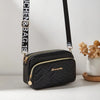 Black quilted crossbody camera bag with a gold letter strap resting on a white surface.
