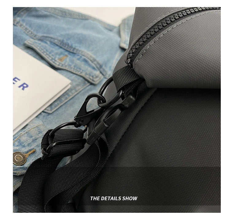 A close-up of a black travel tote bag featuring a zippered compartment and black strap details against a denim background.